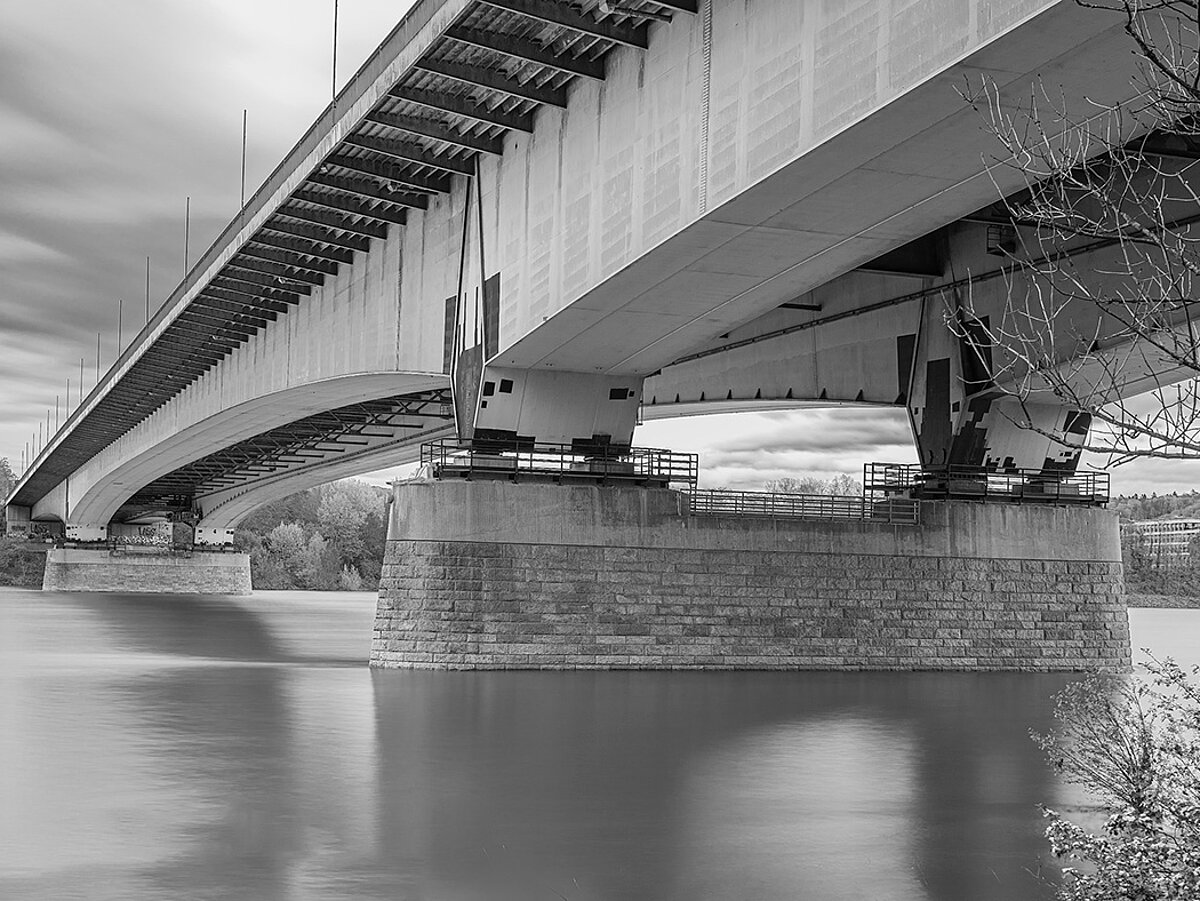 Eine Brücke über einem Fluss. Die Fotografie ist in schwarz-weiß.