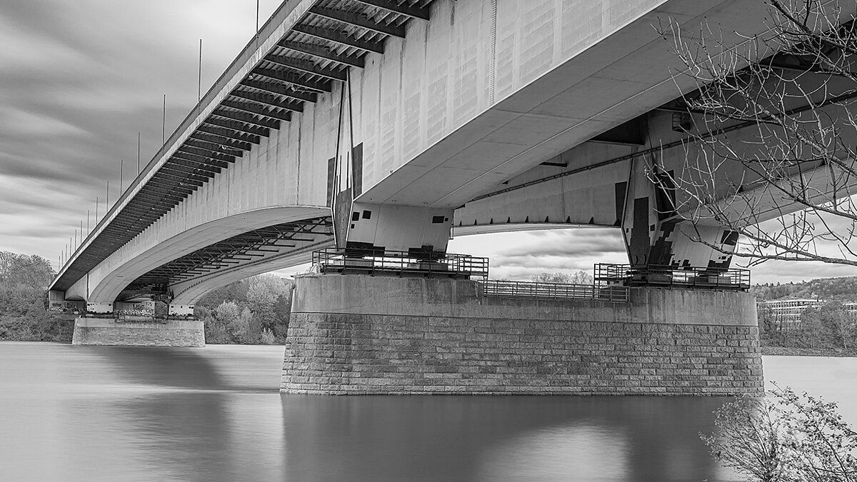 Eine Brücke über einem Fluss. Die Fotografie ist in schwarz-weiß.