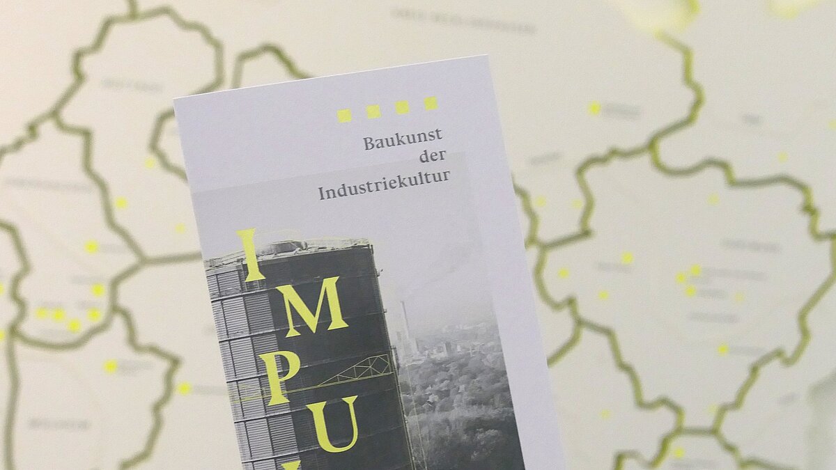 Ein Flyer mit Aufschrift, dahinter eine Wand mit einem Landkarten-Element.