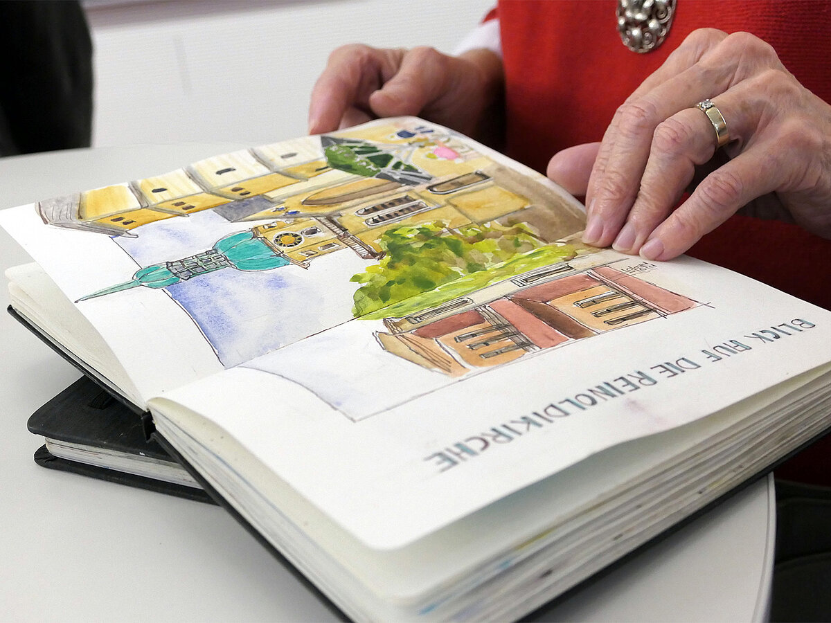 Ein ausgelegtes Skizzenbuch. Eine Person blättert in dem Skizzenbuch.