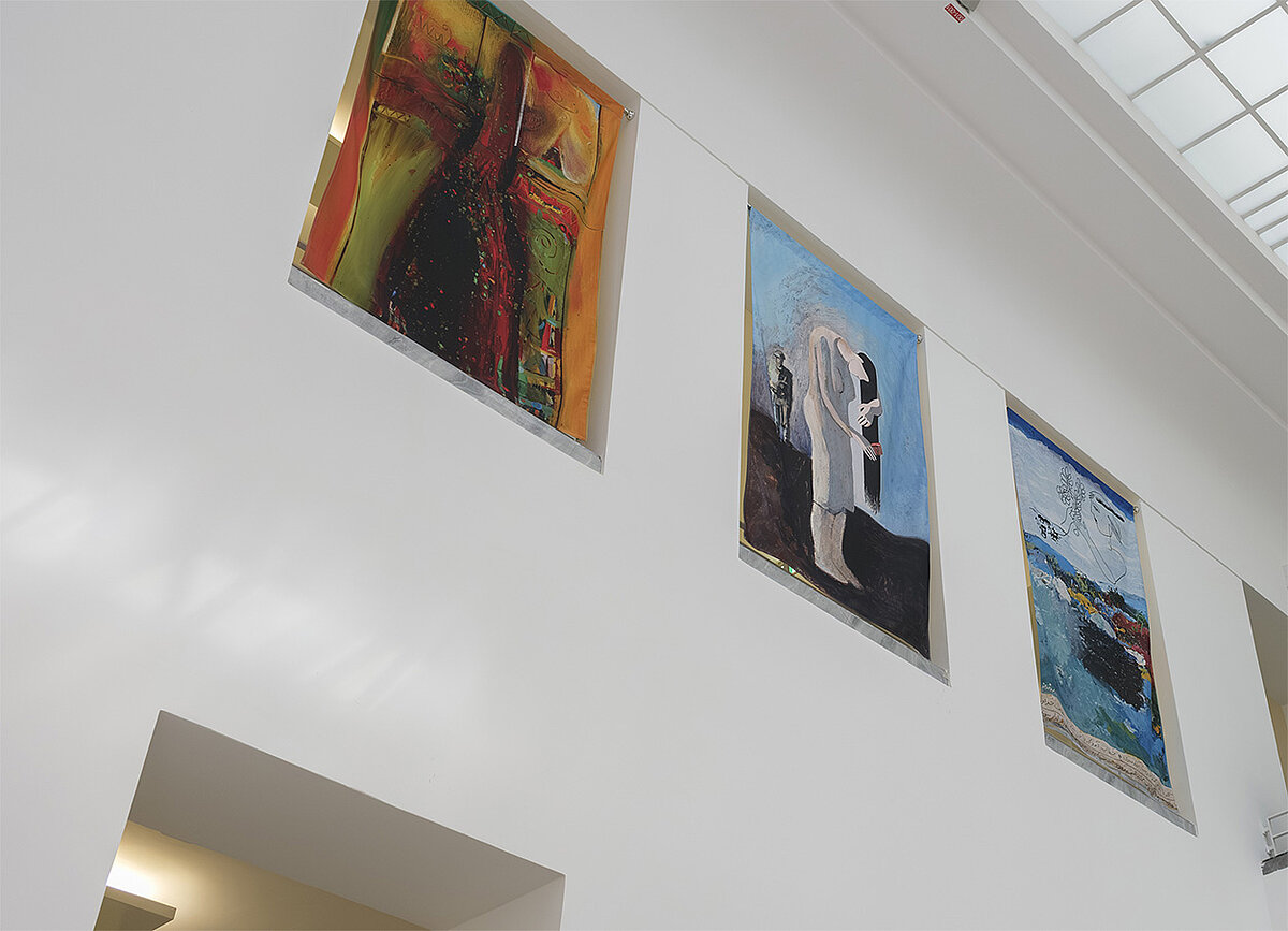 Ein Ausstellungsraum mit bunten Gemälden an den Wänden.