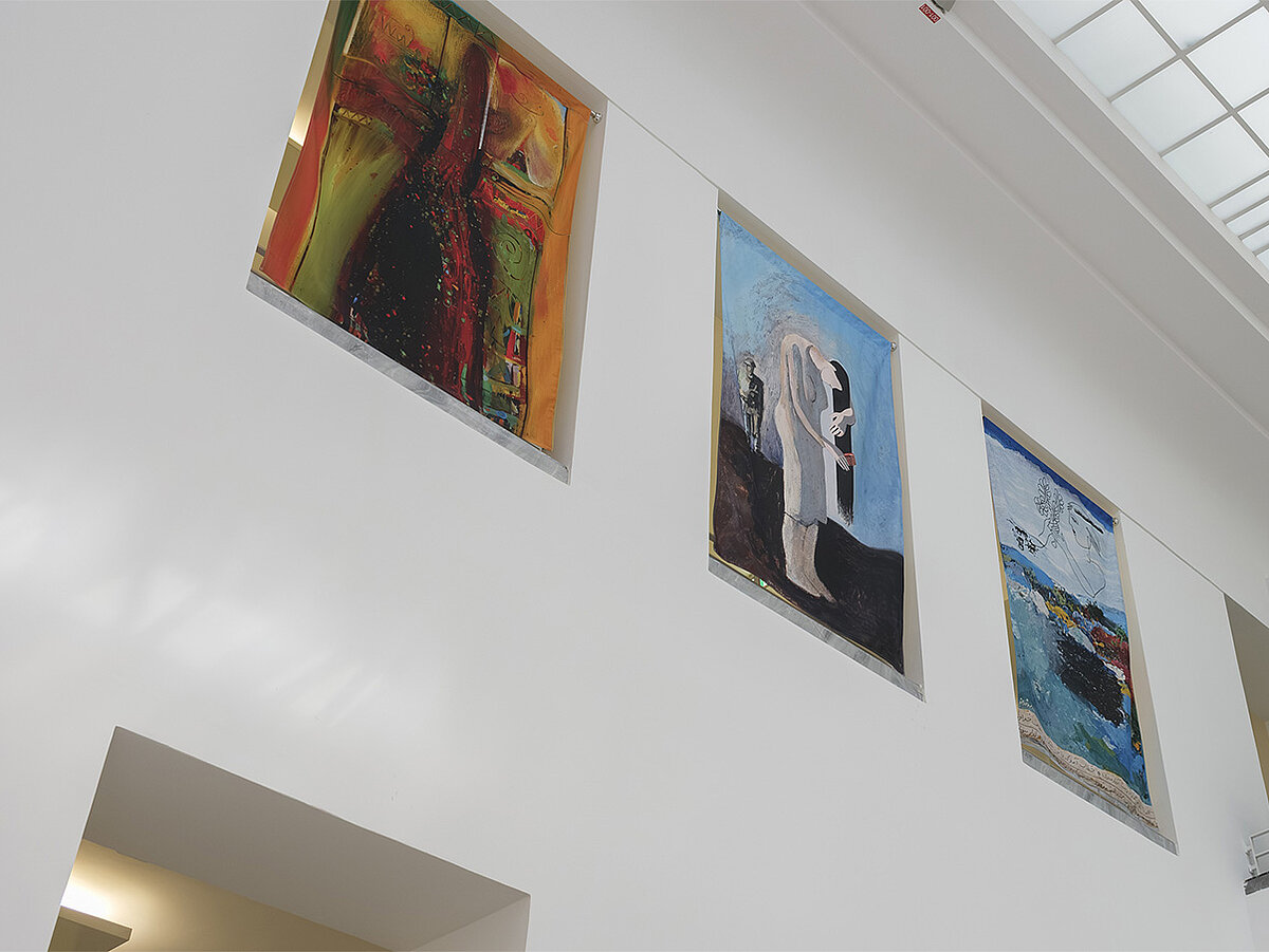Ein Ausstellungsraum mit bunten Gemälden an den Wänden.