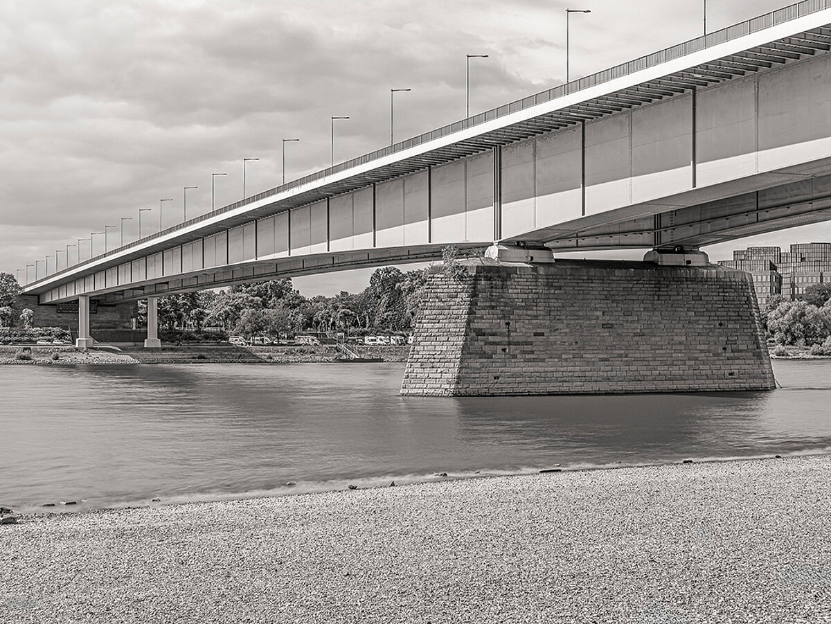 Eine Brücke über einem Fluss. Die Fotografie ist in schwarz-weiß gehalten.