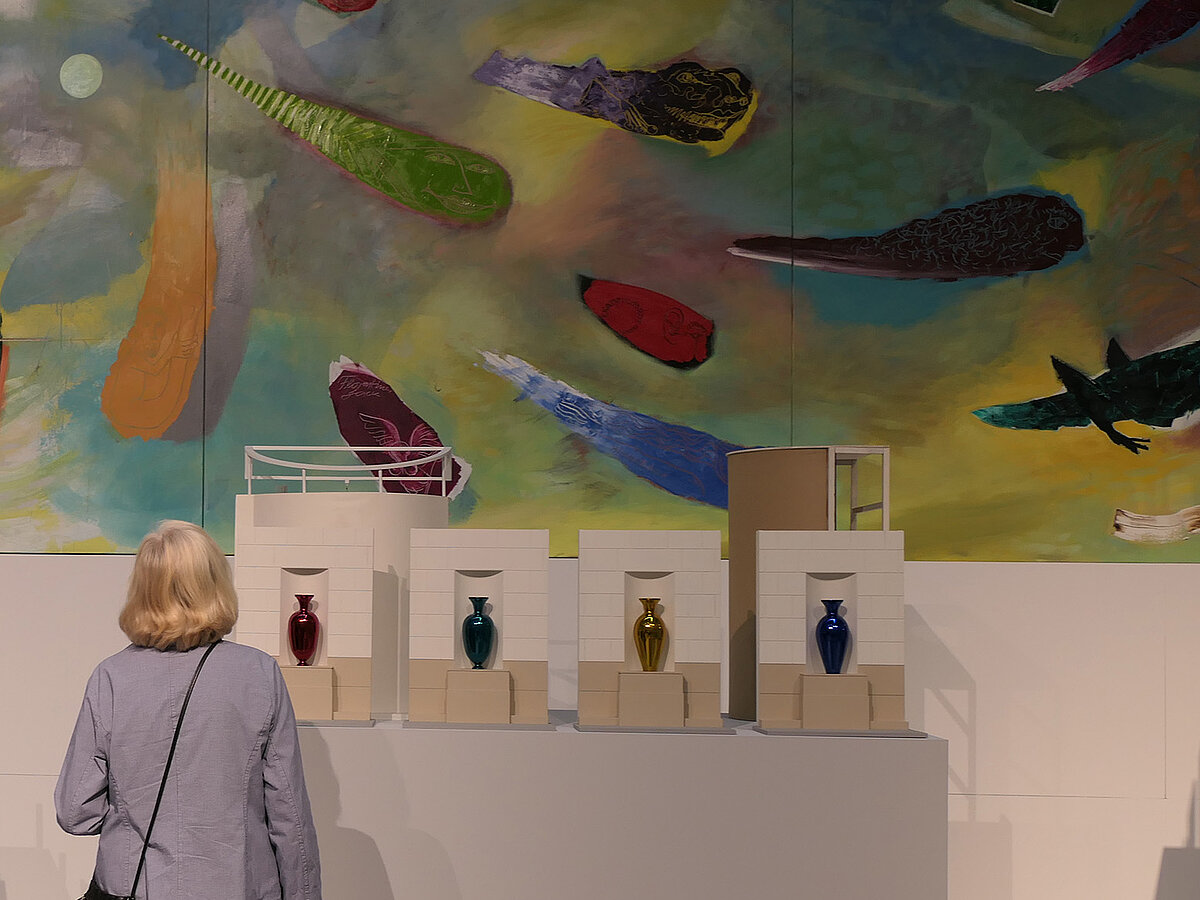 Eine Person steht in einer Ausstellung und betrachtet Skulpturen und Gemälde.