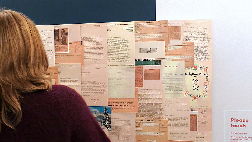Eine Pinwand mit Dokumenten an einer Wand, davor steht eine Person, man erkennt den Rücken im Anschnitt.