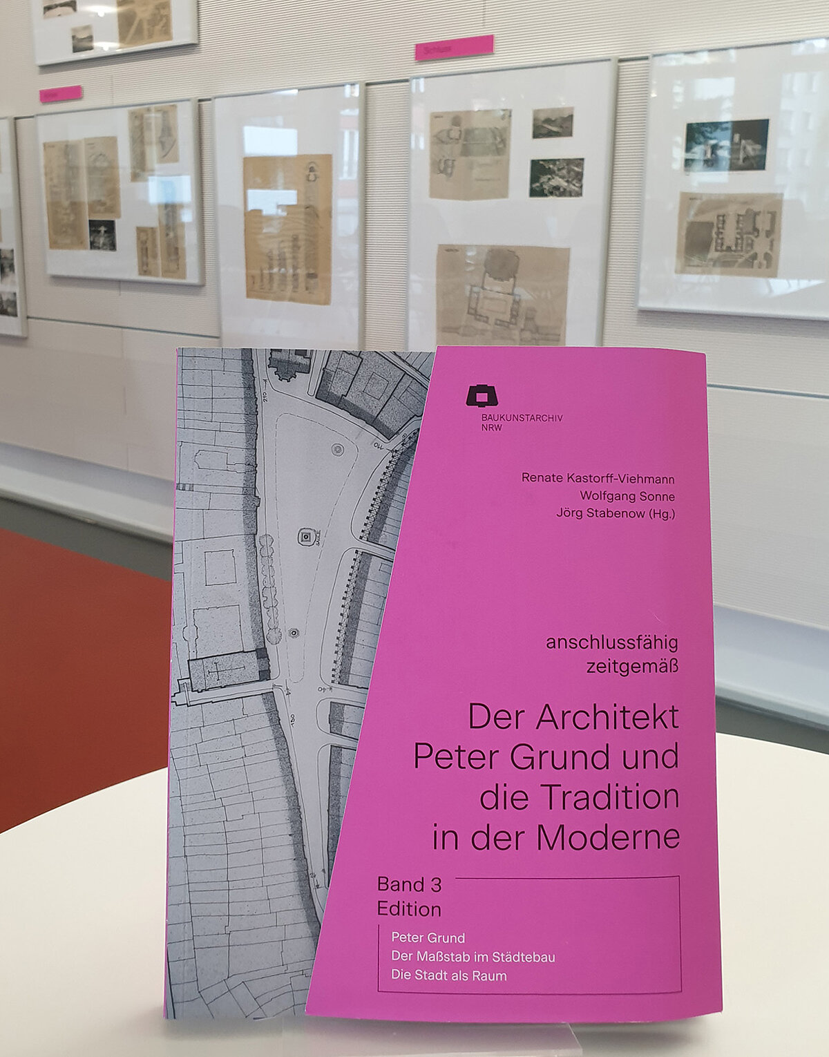 Eine Publikation steht auf einem Tisch, dahinter ist eine Wand mit Text- und Bildttafeln.