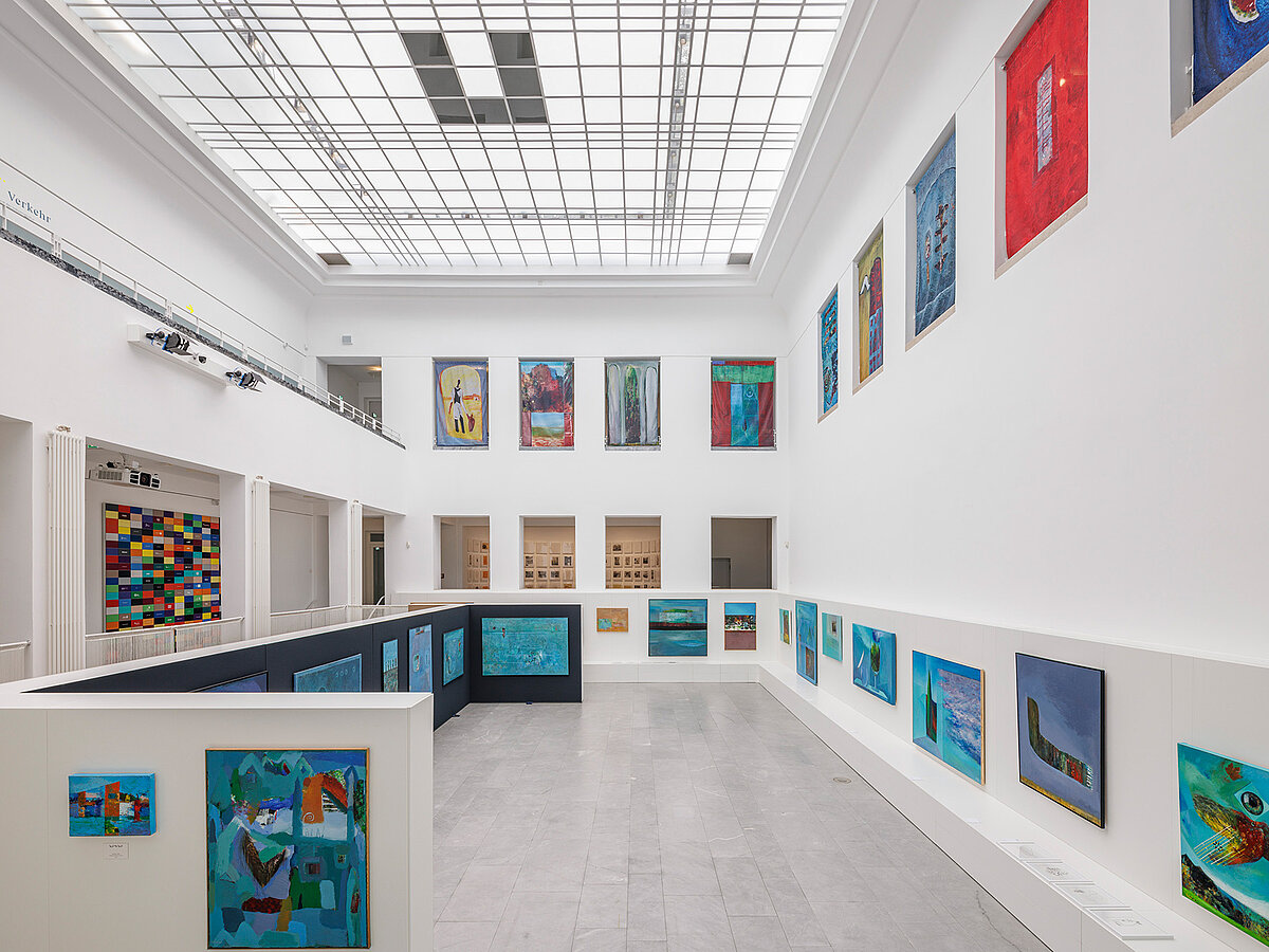 Lichtdurchfluteter Ausstellungsraum mit vielfältigen, bunten Gemälden.