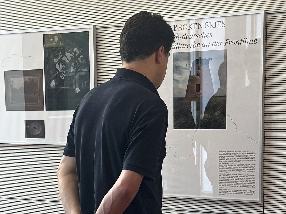 Eine Person in einer Ausstellung. Die Person betrachtet Foto- und Texttafeln.