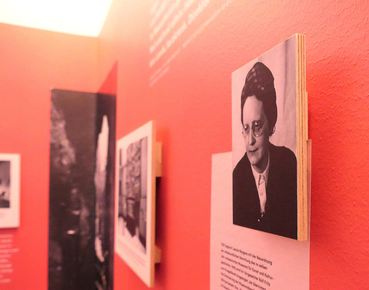 Eine rötlich gefärbte Wand, darauf sind Texte und Fotos abgebildet und aufgehangen.