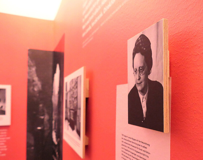 Eine rötlich gefärbte Wand, darauf sind Texte und Fotos abgebildet und aufgehangen.