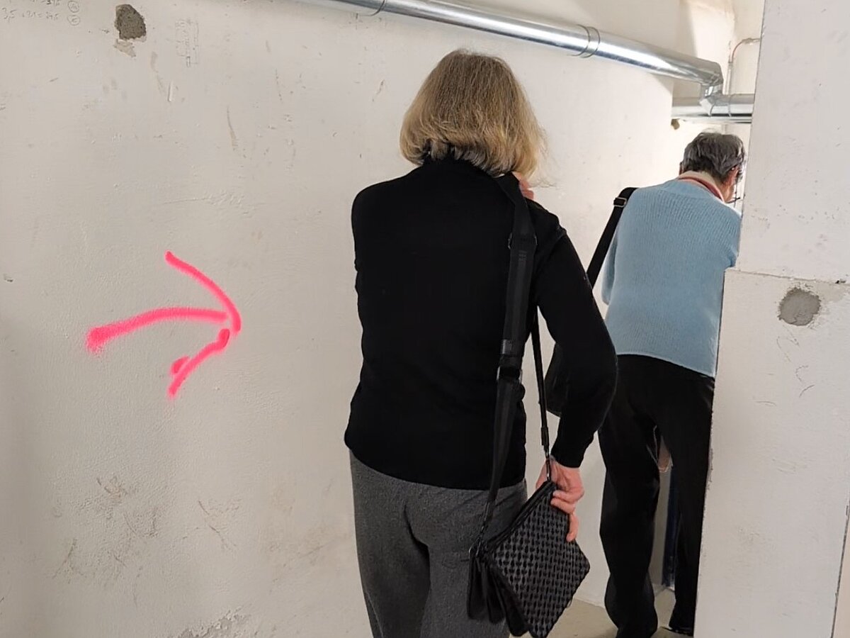 Personen gehen einen Flur entlang, an der Wand ist ein pinker Pfeil.