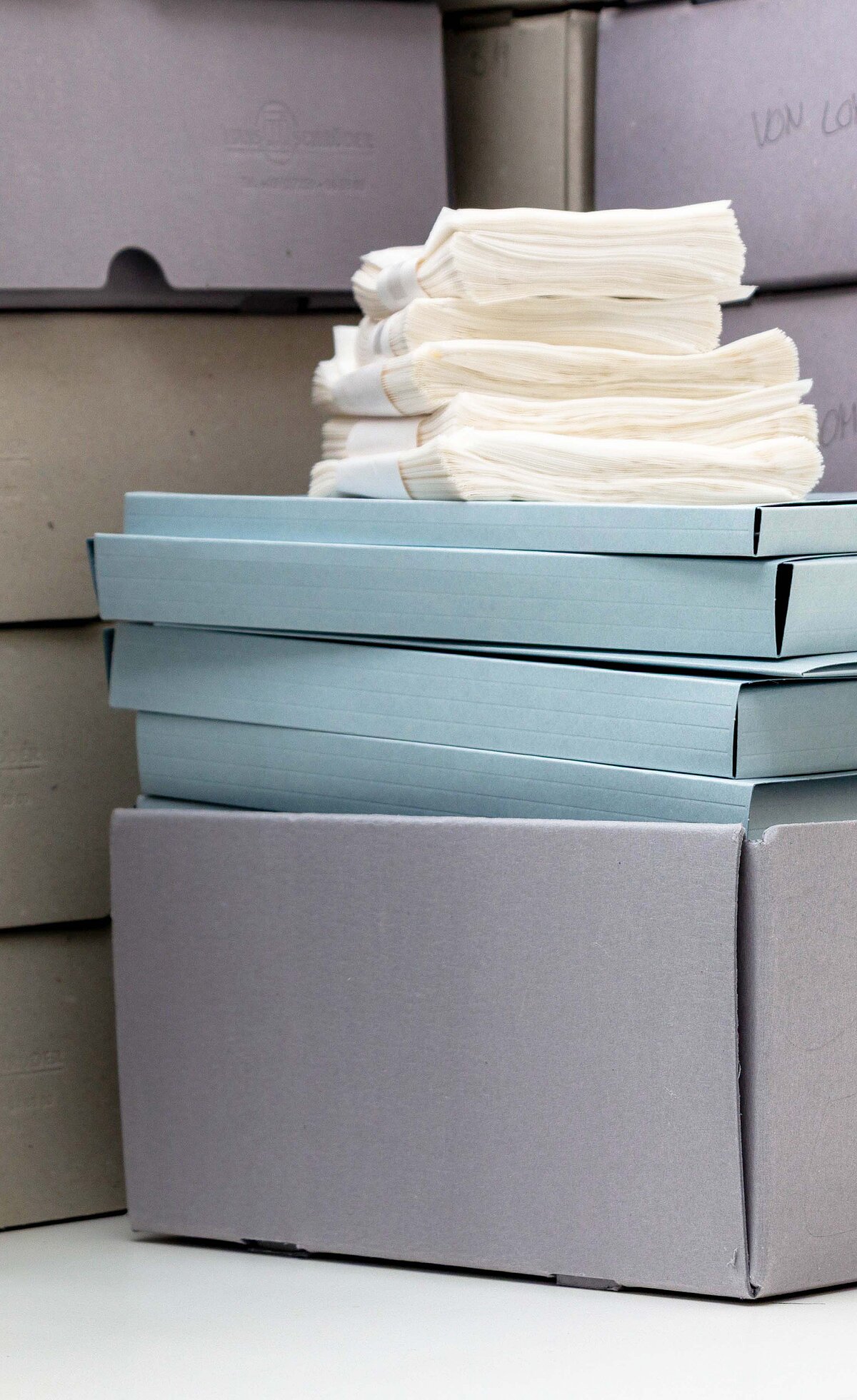 Graue sowie hellblaue Boxen und helle Dokumente liegen gestapelt nebeneinander und teilweise übereinander. -  Foto: Christine Kämmerer/Baukunstarchiv NRW