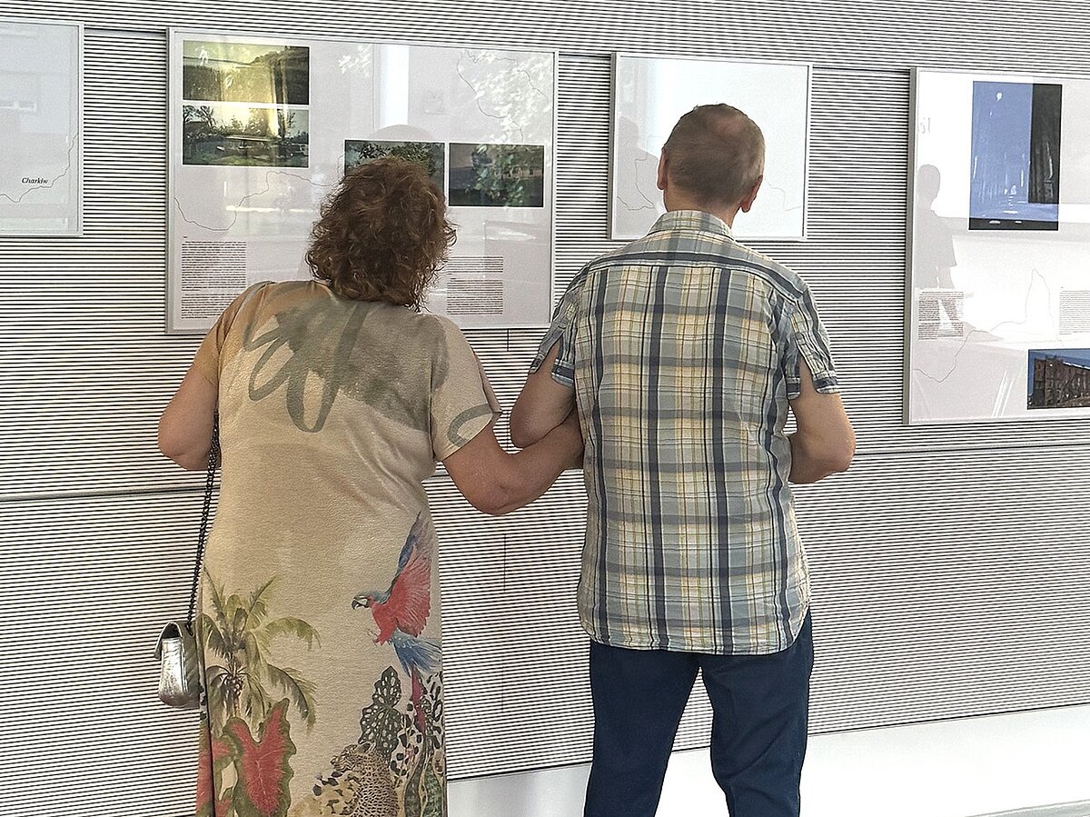 Zwei Personen stehen in einer Ausstellung und betrachten Foto- und Texttafeln.
