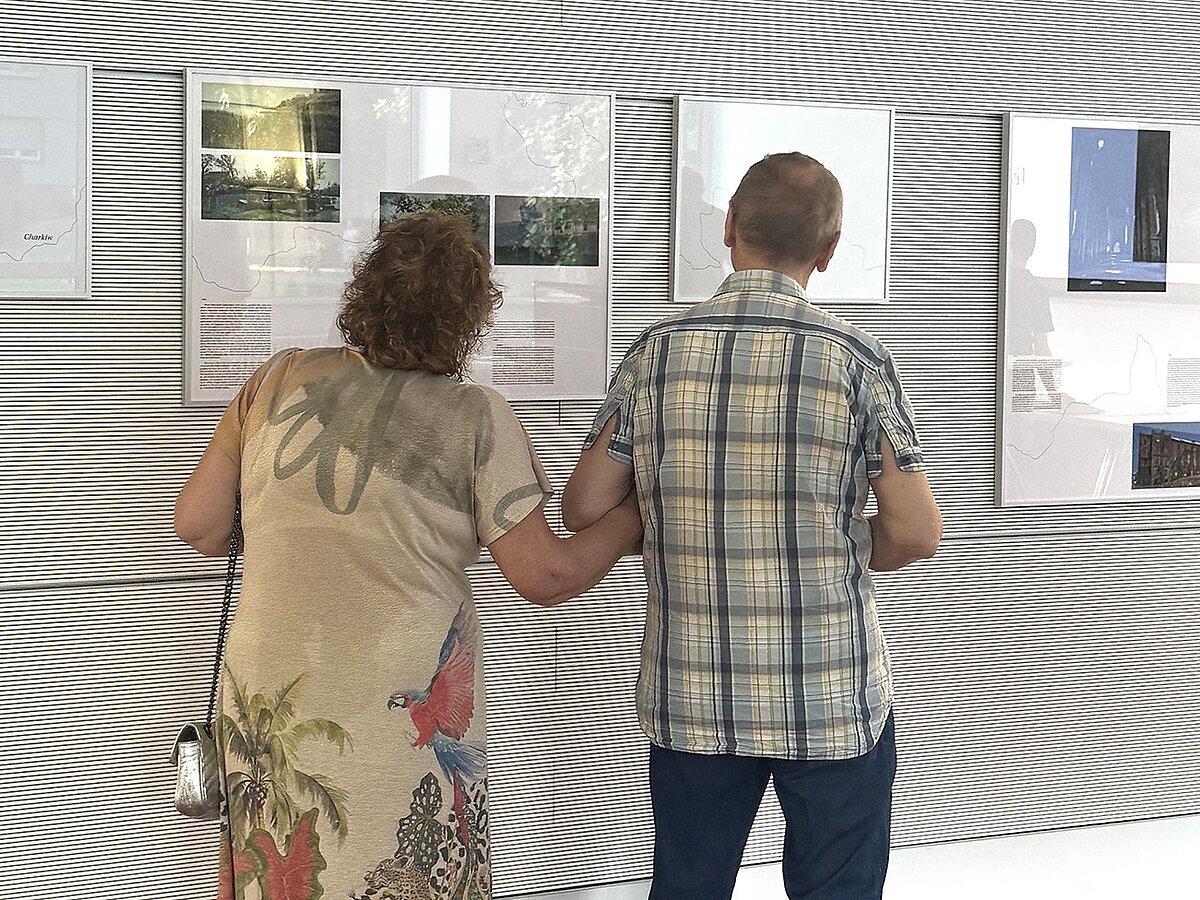 Zwei Personen stehen in einer Ausstellung und betrachten Foto- und Texttafeln.