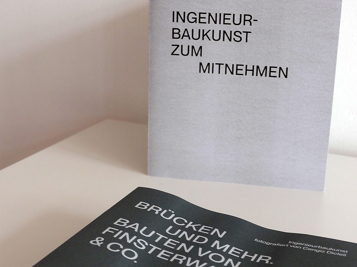 Eine Broschüre liegt auf einem Tisch, dahinter steht ein Schild mit Aufschrift.