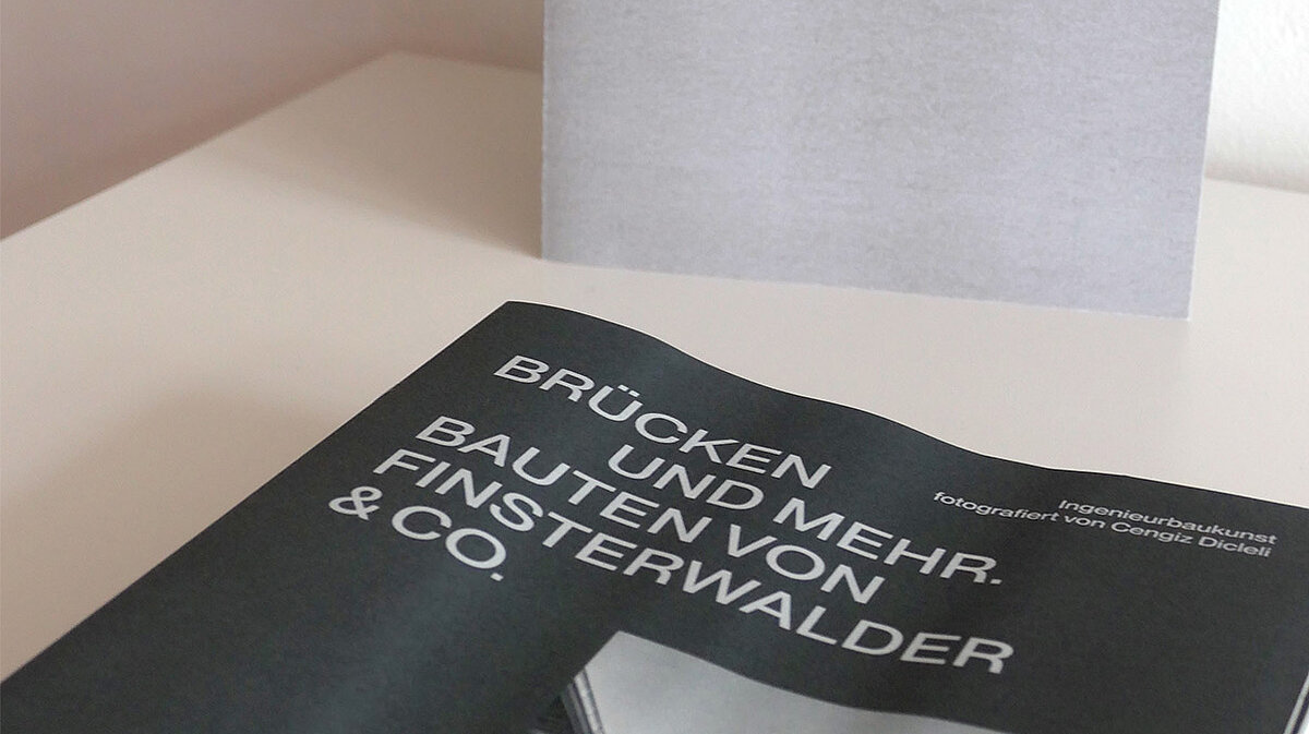 Eine Broschüre liegt auf einem Tisch, dahinter steht ein Schild mit Aufschrift.