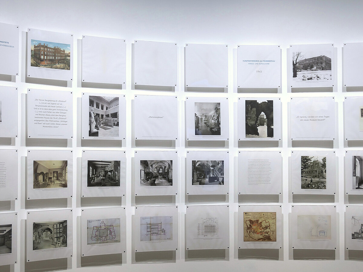 Eine weiße Wand, daran sind Foto- und Texttafeln befestigt.