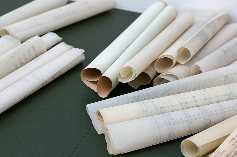 Baupläne aus Papier liegen aufgerollt nebeneinander.